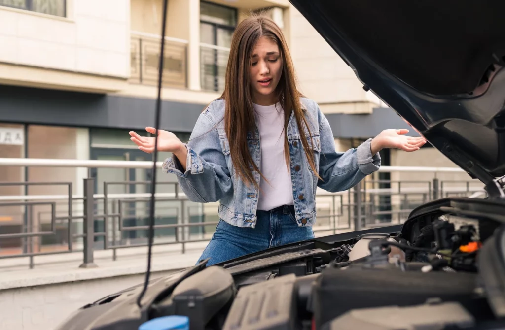 young worried girl is using a phone to explain the mechanic the problem with a car that she has